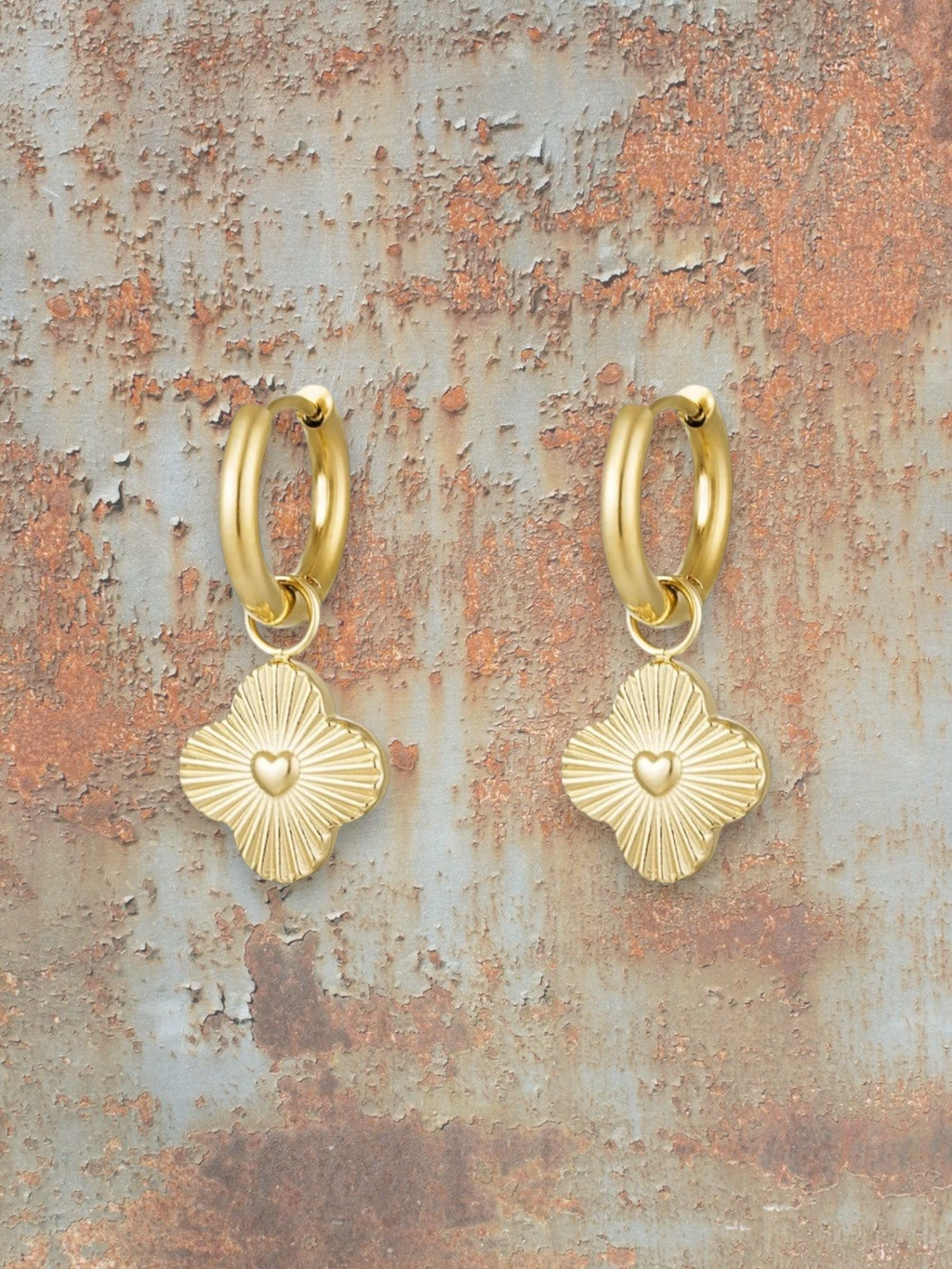 WILDSIDE gold-plated metal hoop earrings with clover charms featuring embossed hearts and radiating lines.