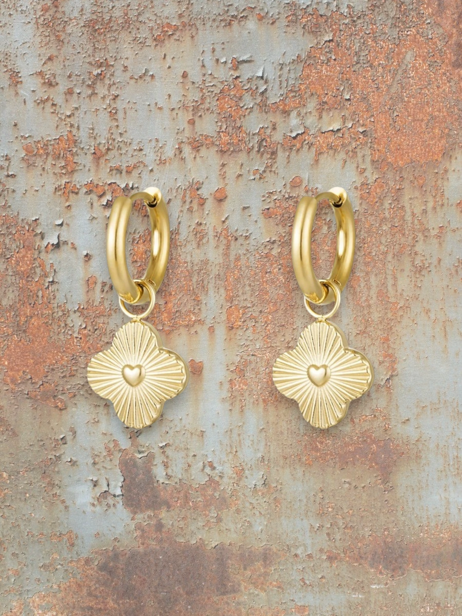 WILDSIDE gold-plated metal hoop earrings with clover charms featuring embossed hearts and radiating lines.