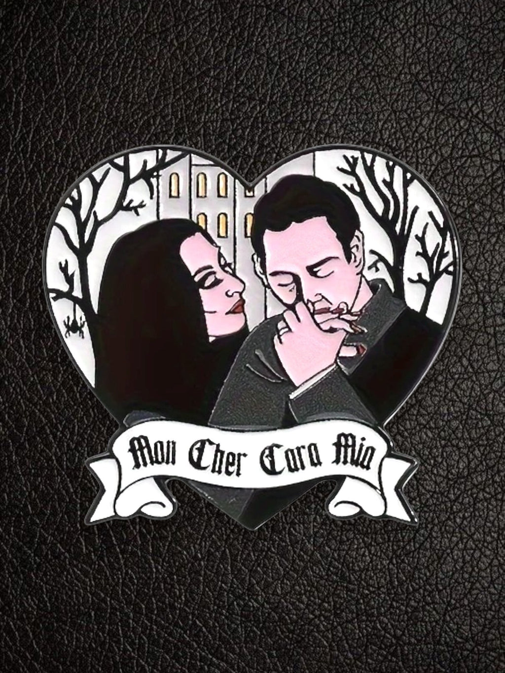 WILDSIDE Addams Family heart-shaped enamel pin featuring Morticia and Gomez with a gothic house and trees. "Mon Cher Cara Mia" banner.