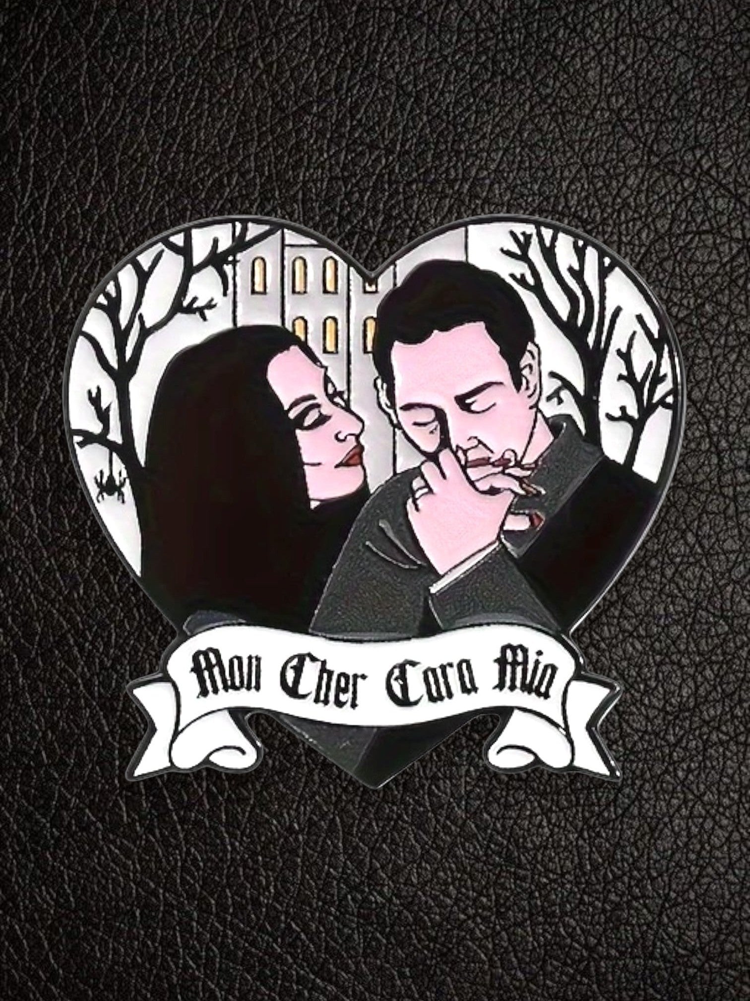 WILDSIDE Addams Family heart-shaped enamel pin featuring Morticia and Gomez with a gothic house and trees. "Mon Cher Cara Mia" banner.