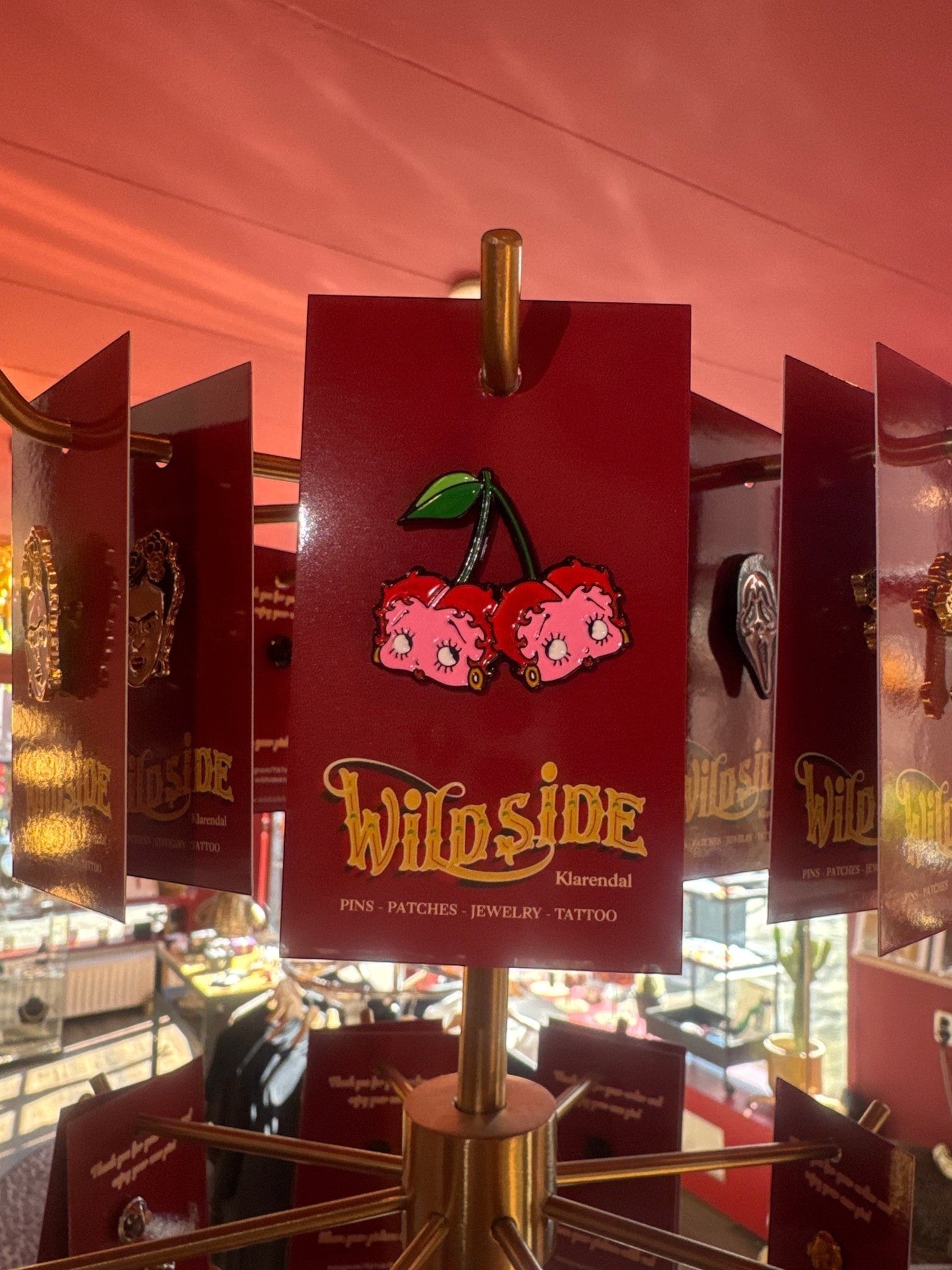 WILDSIDE Betty Boop cherry enamel pin with green stem and leaves. Pink cherries with large eyes and eyelashes.