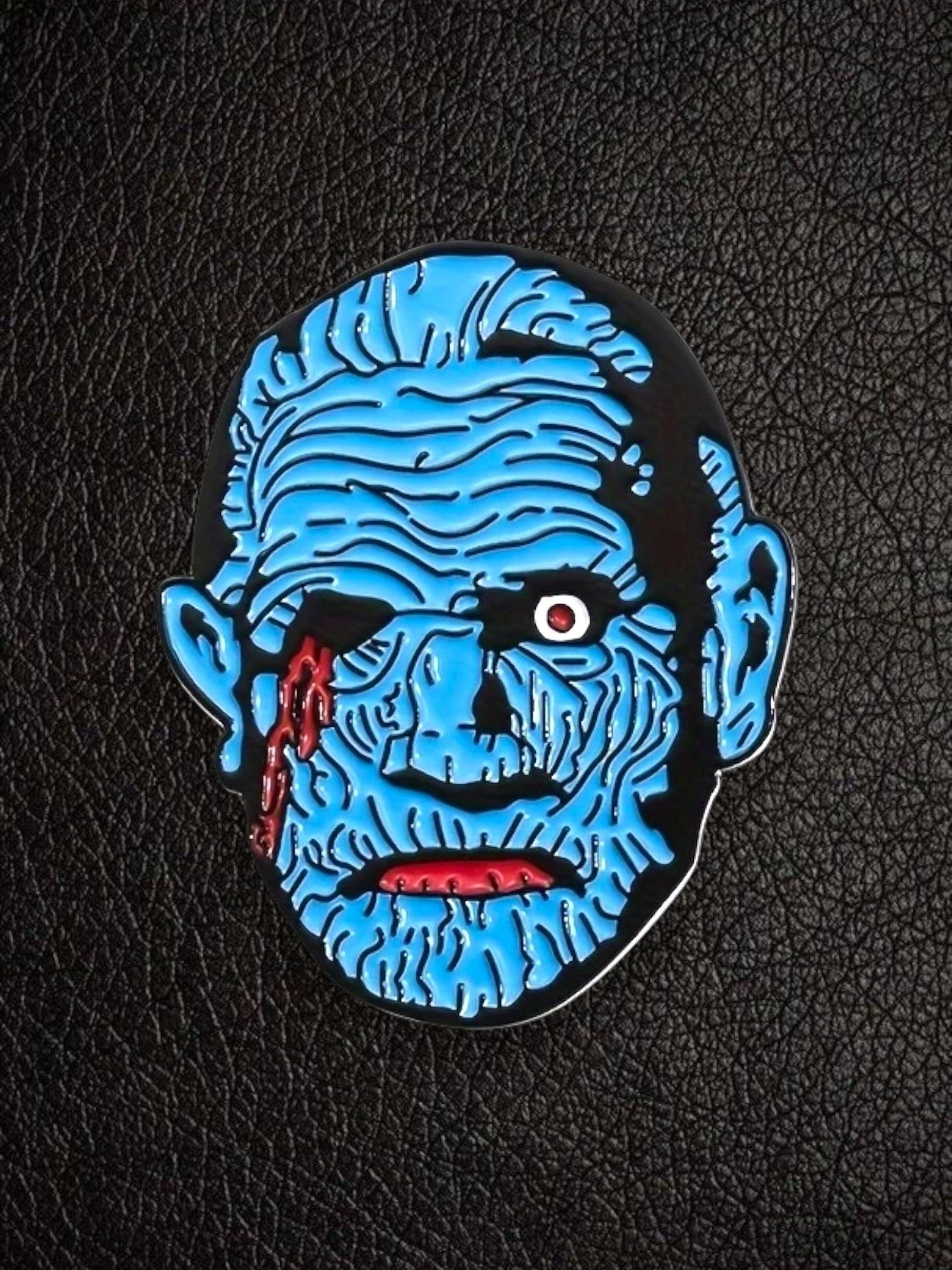 WILDSIDE blue monster enamel pin with red accents and black outline, on a black textured background.