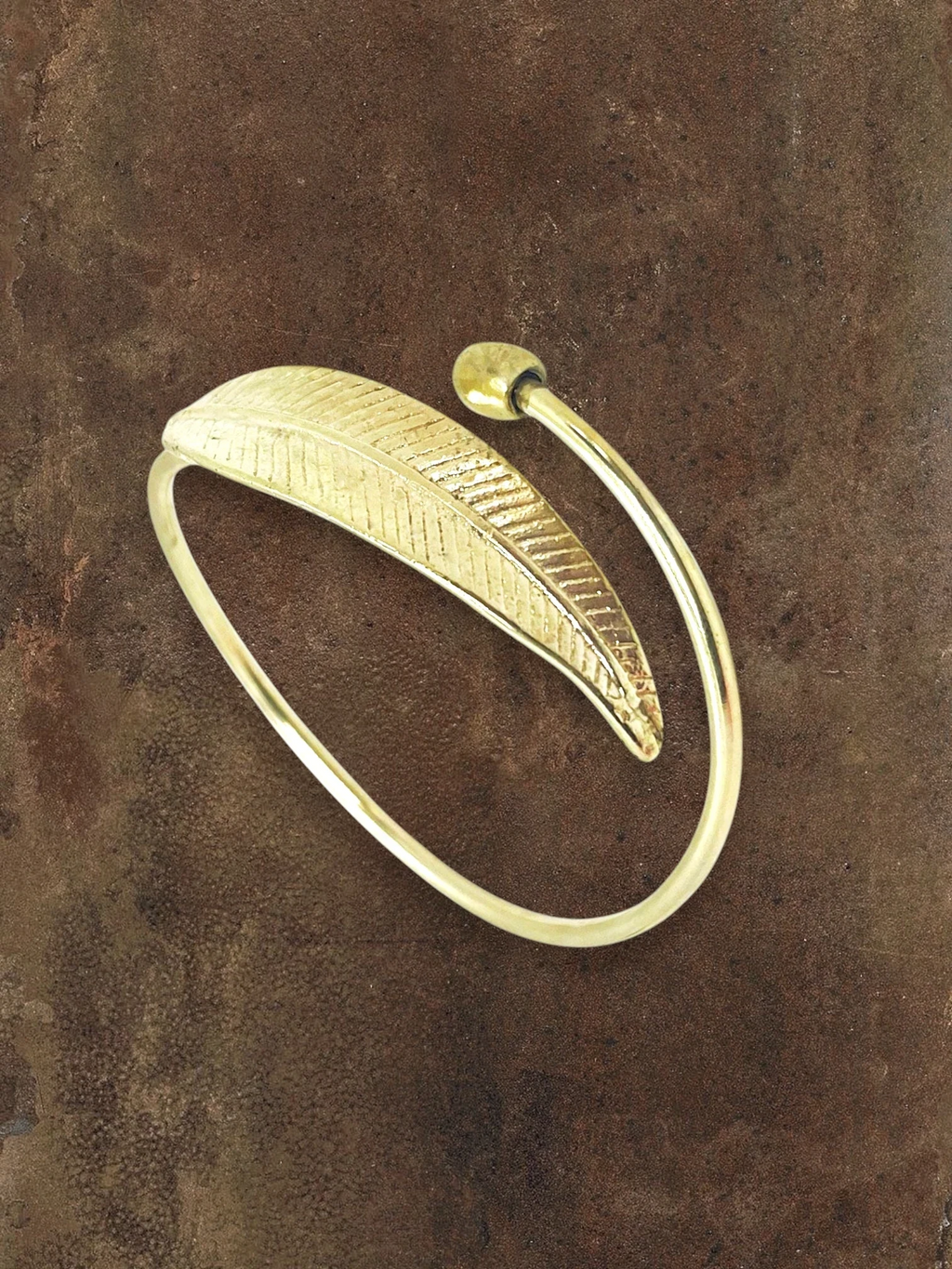 WILDSIDE polished brass open cuff bracelet featuring a detailed organic leaf design on a textured brown background.