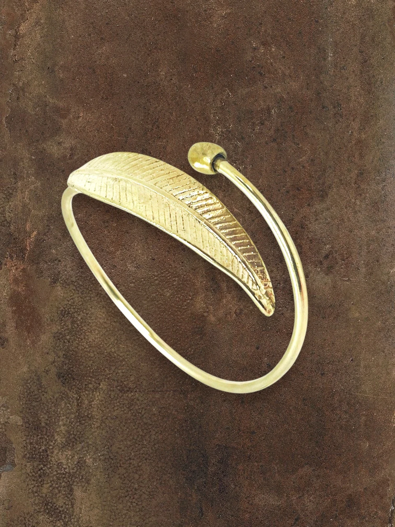 WILDSIDE polished brass open cuff bracelet featuring a detailed organic leaf design on a textured brown background.