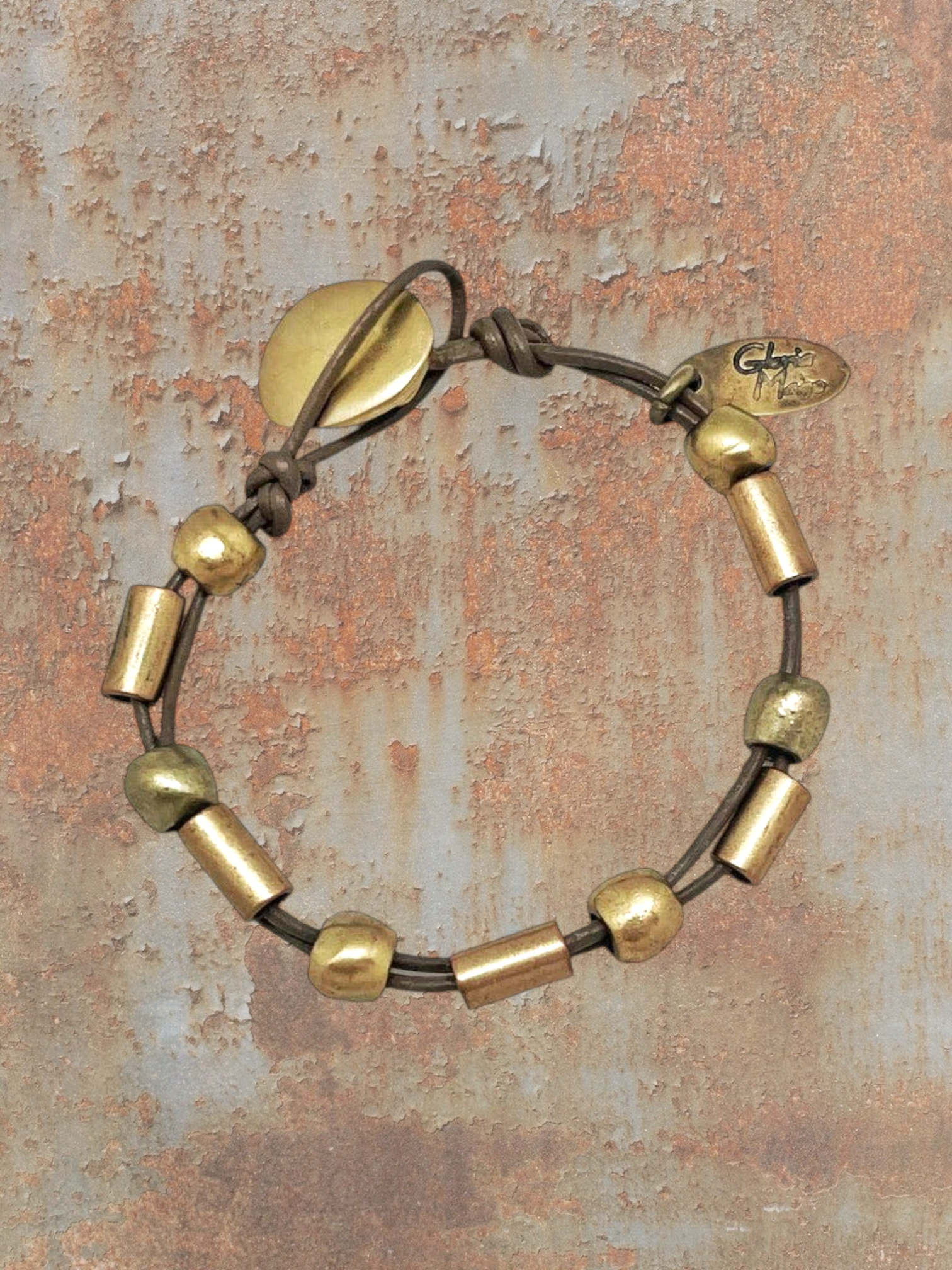 WILDSIDE brown leather bracelet with gold-tone beads and a knot closure. Features a leaf-shaped charm and a small oval brand tag.