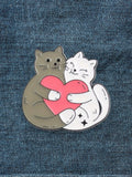 WILDSIDE enamel pin of two cats, one grey and one white, hugging a pink heart.