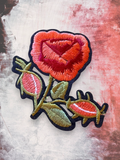 WILDSIDE embroidered patch of a red and orange rose with green leaves and buds. Features a black border.