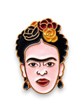 WILDSIDE Frida Kahlo enamel pin with gold trim, featuring pink face, black hair, floral crown, and blue teardrop earrings.