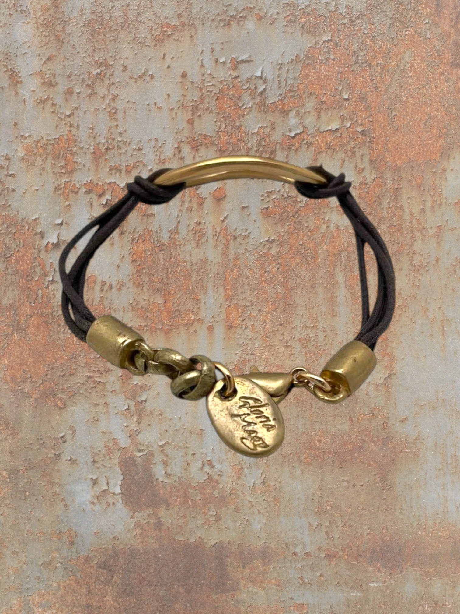 WILDSIDE bracelet with brown cord, gold bar accent, and oval charm. Adjustable clasp.
