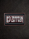 WILDSIDE Led Zeppelin rectangular enamel pin with white and red lettering on a black background with a copper-colored border.