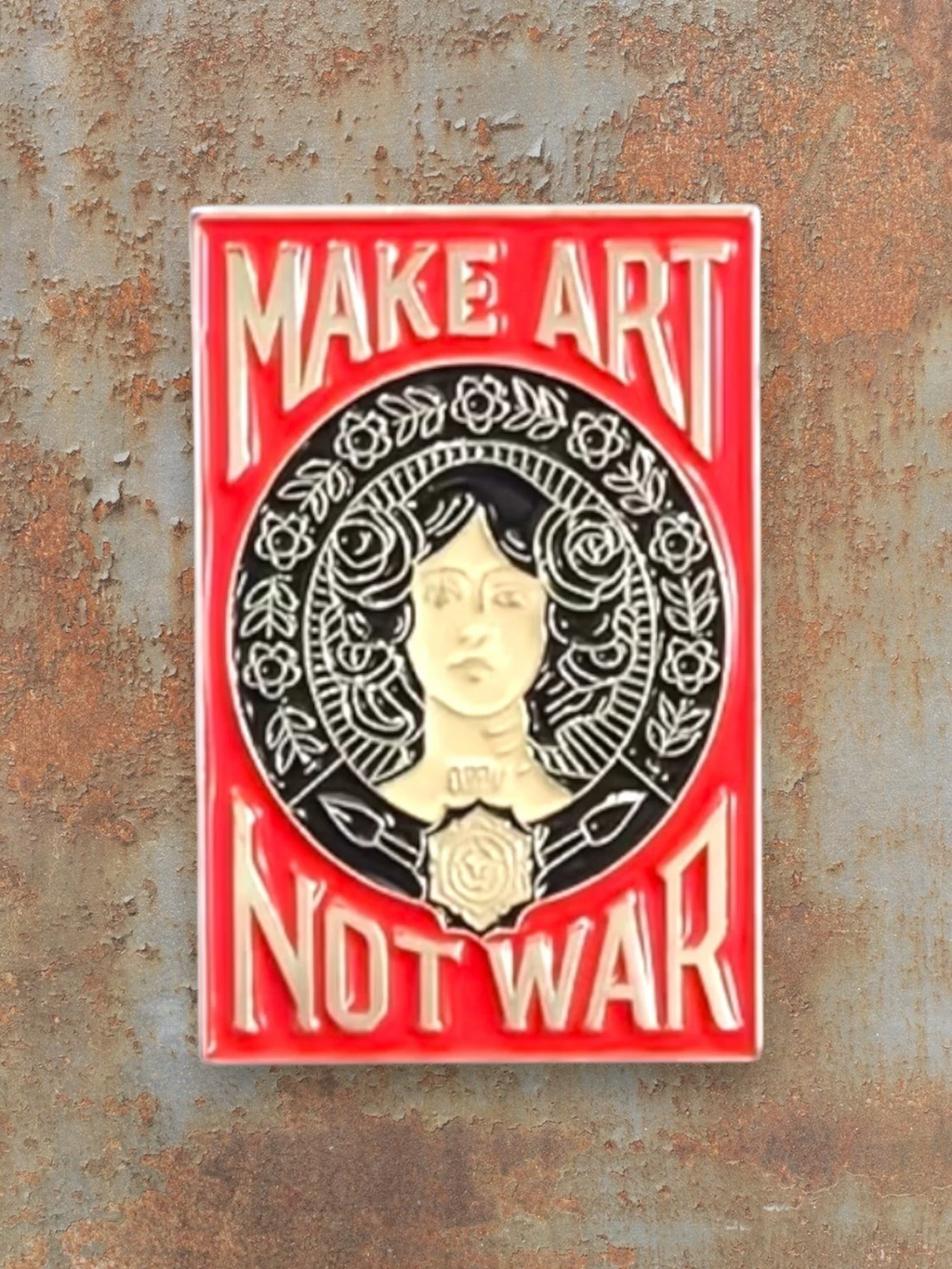 WILDSIDE enamel pin with red background, featuring a woman's face surrounded by roses and the text "MAKE ART NOT WAR".