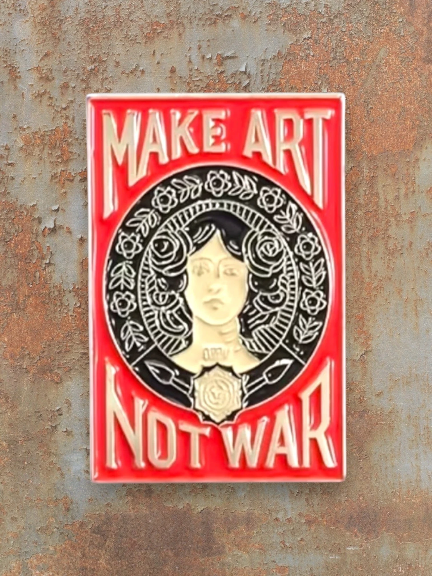 WILDSIDE enamel pin with red background, featuring a woman's face surrounded by roses and the text "MAKE ART NOT WAR".