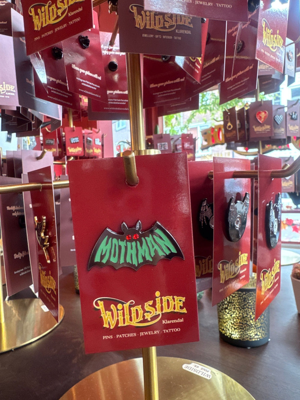 WILDSIDE Mothman enamel pin with green lettering and red gem eyes on a red backing card.