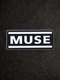 WILDSIDE black rectangular pin with white text spelling MUSE, featuring two white horizontal lines above and below the text.