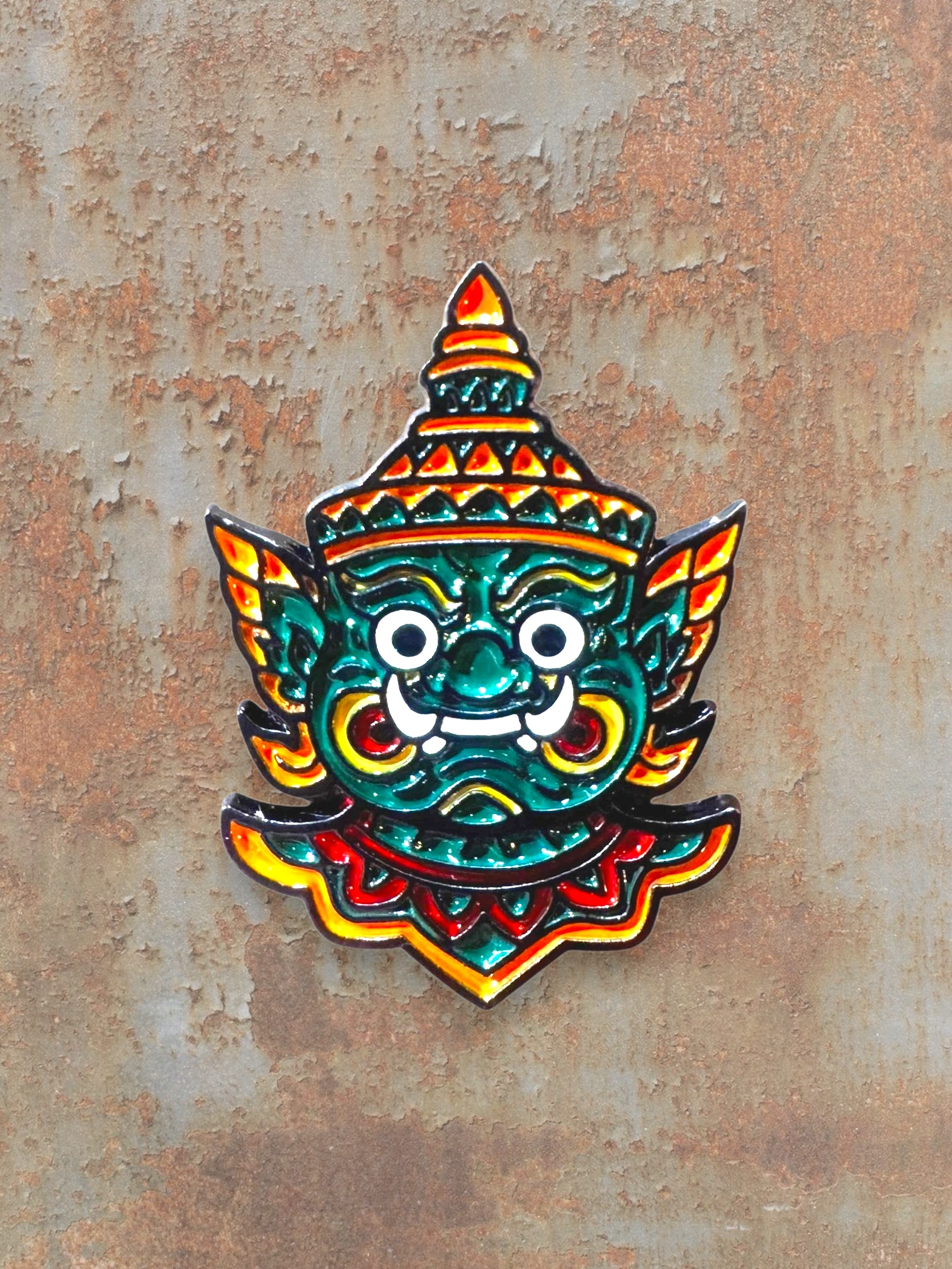 WILDSIDE enamel pin featuring a green mythical creature mask with a red and yellow headdress and ornate details.