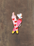 WILDSIDE pink enamel pin featuring two crossed joints with red hearts and white hearts at the tips. Rose gold trim.