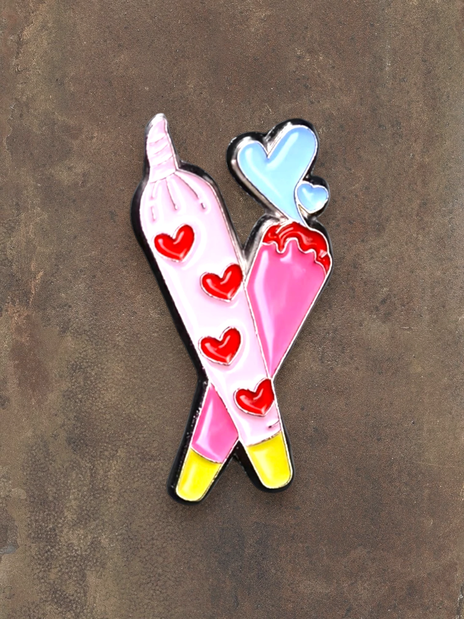 WILDSIDE pink enamel pin with red hearts and blue hearts, shaped like crossed joints.