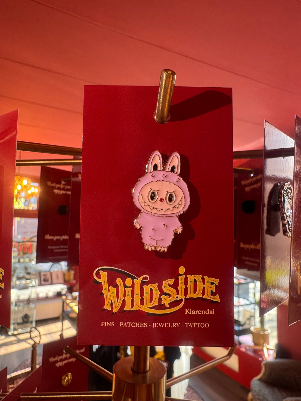 WILDSIDE pink monster enamel pin with big eyes and sharp teeth, featuring bunny ears.