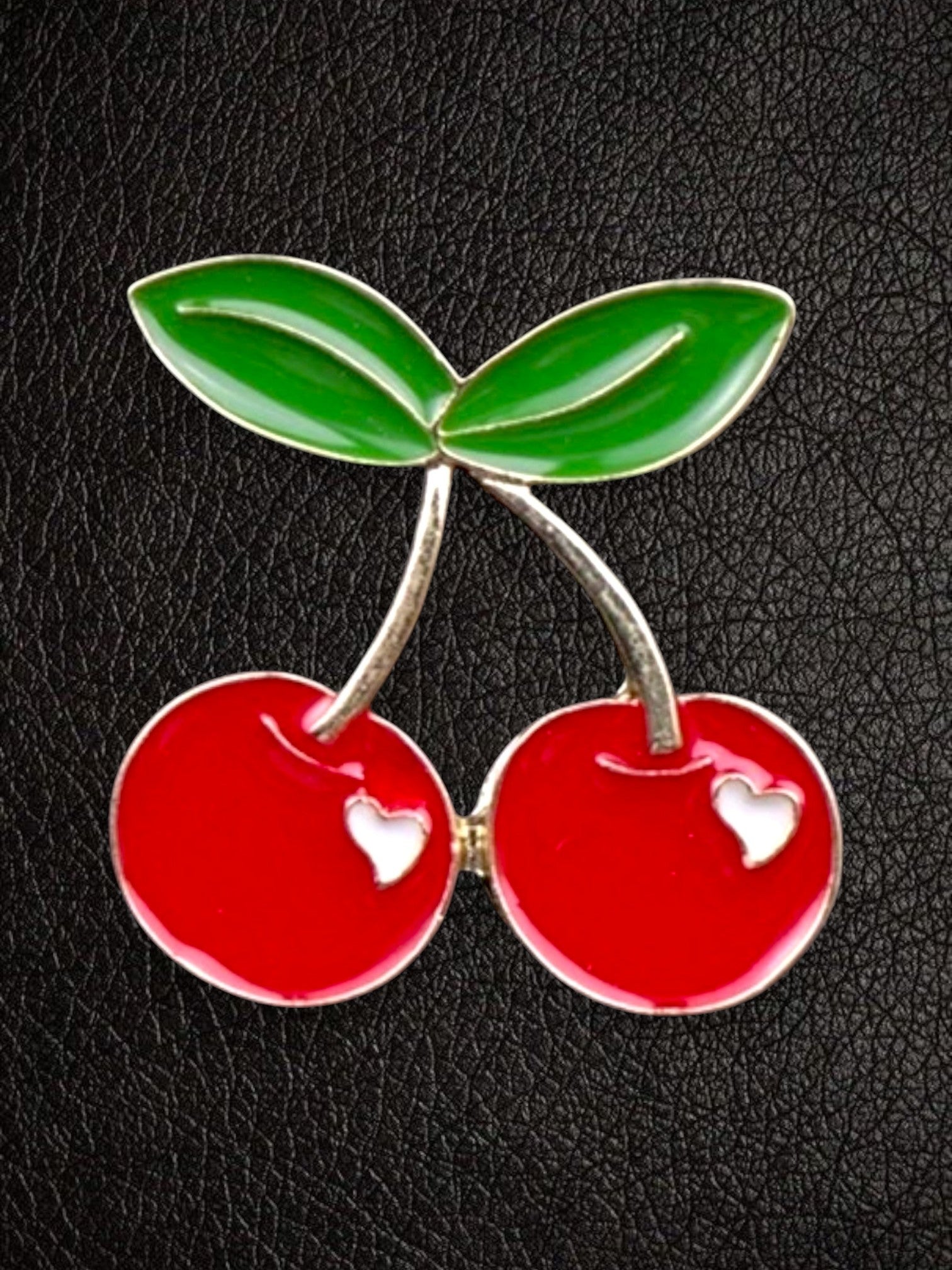 WILDSIDE red enamel cherry pin with green leaves and white heart cutouts on a black textured background.
