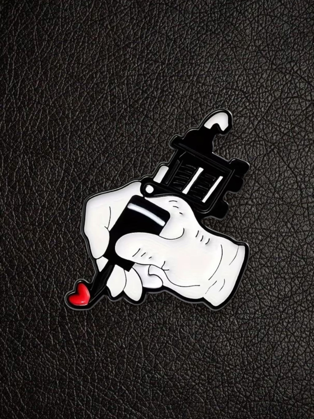 WILDSIDE enamel pin of a white hand holding a black tattoo gun with a red heart detail.