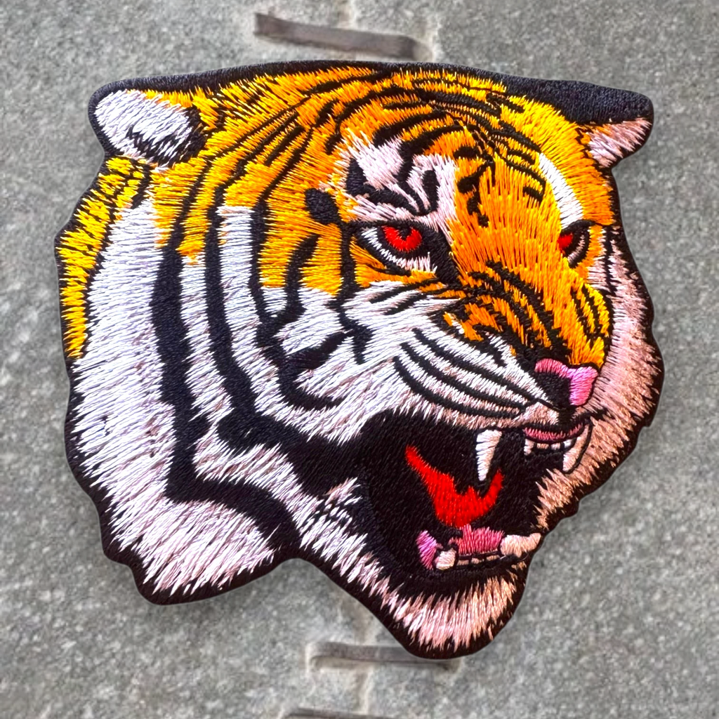 WILDSIDE embroidered patch of a roaring tiger head with orange, white, black, and red details. Features red eyes and pink nose.